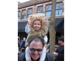 Nolan Wheeler, the 15-month old lion who won the costume contest in his age group, waves from above the shoulders of his father, Ken